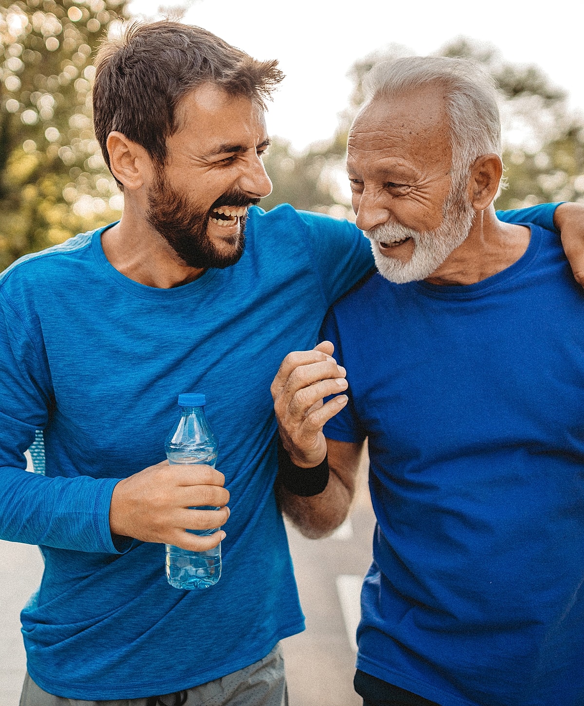 Two men laughing while exercising together outdoors.