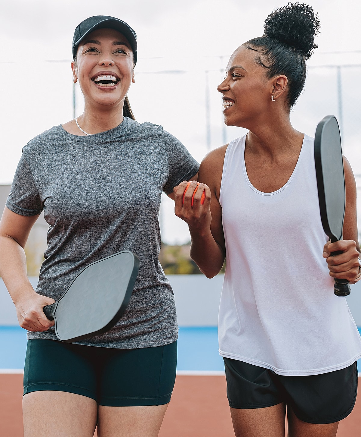 Two women smiling with paddles on court.