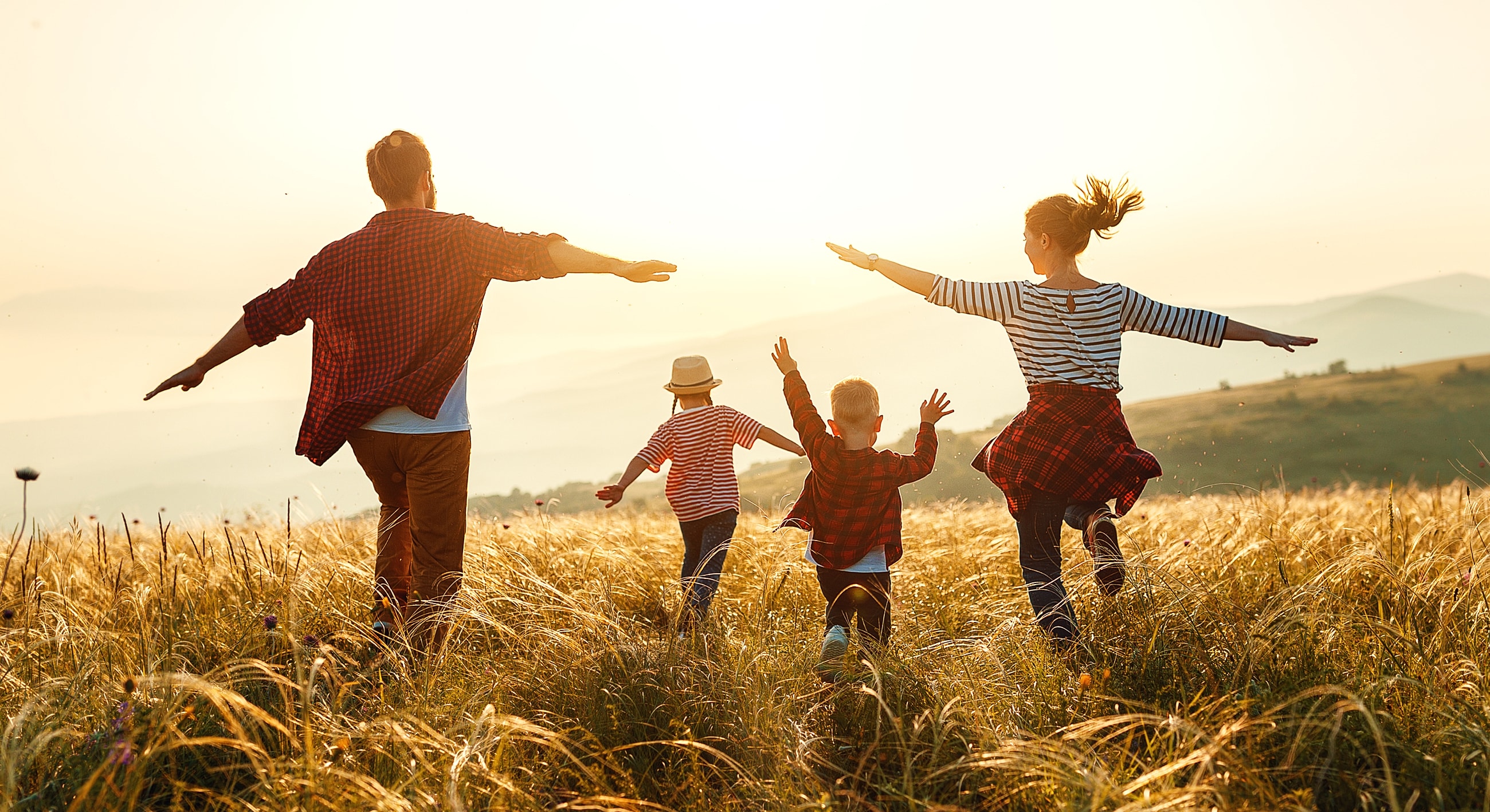 Family running joyfully in a sunlit field.