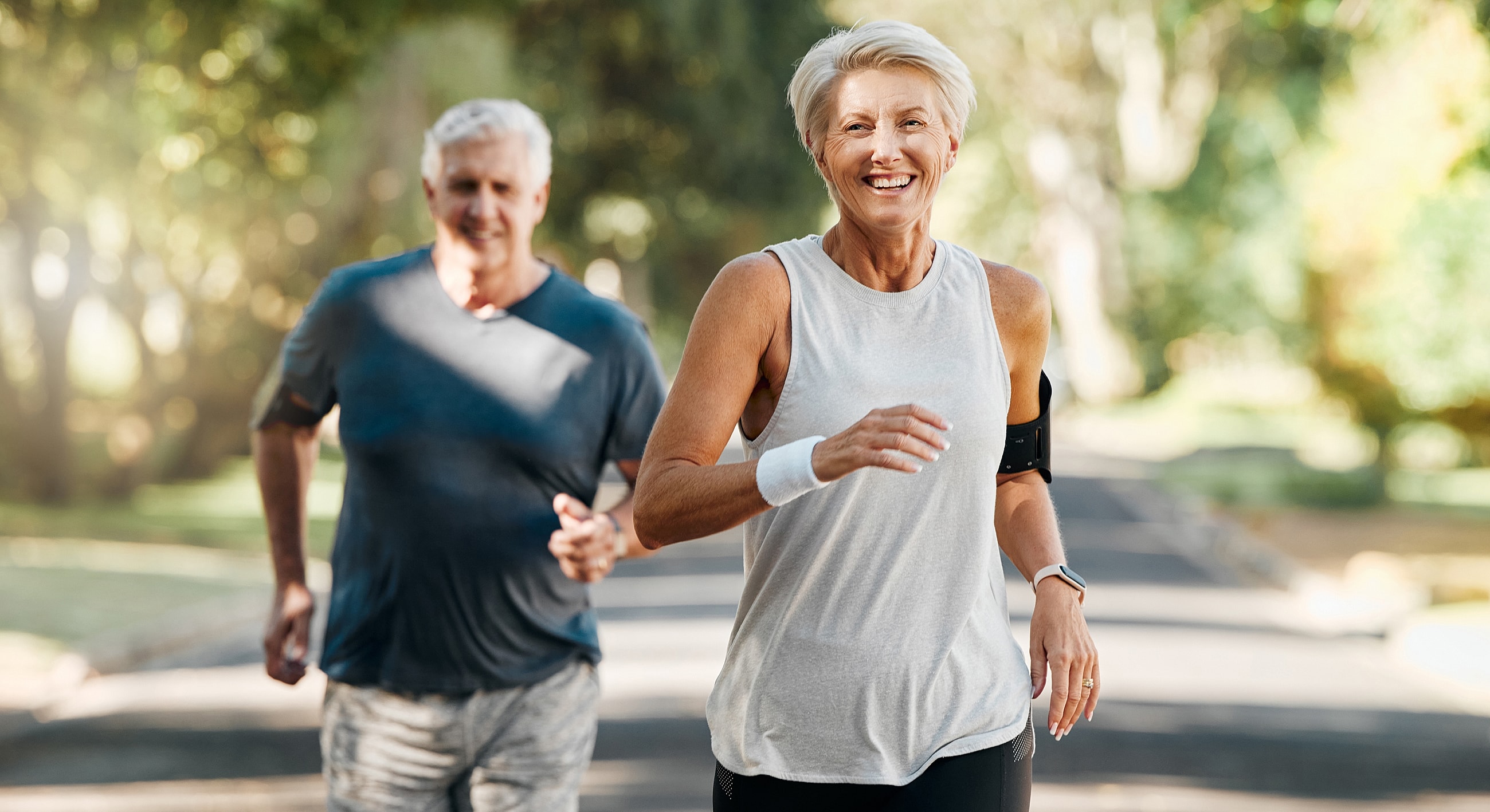 Elderly couple running outdoors in sunny park.