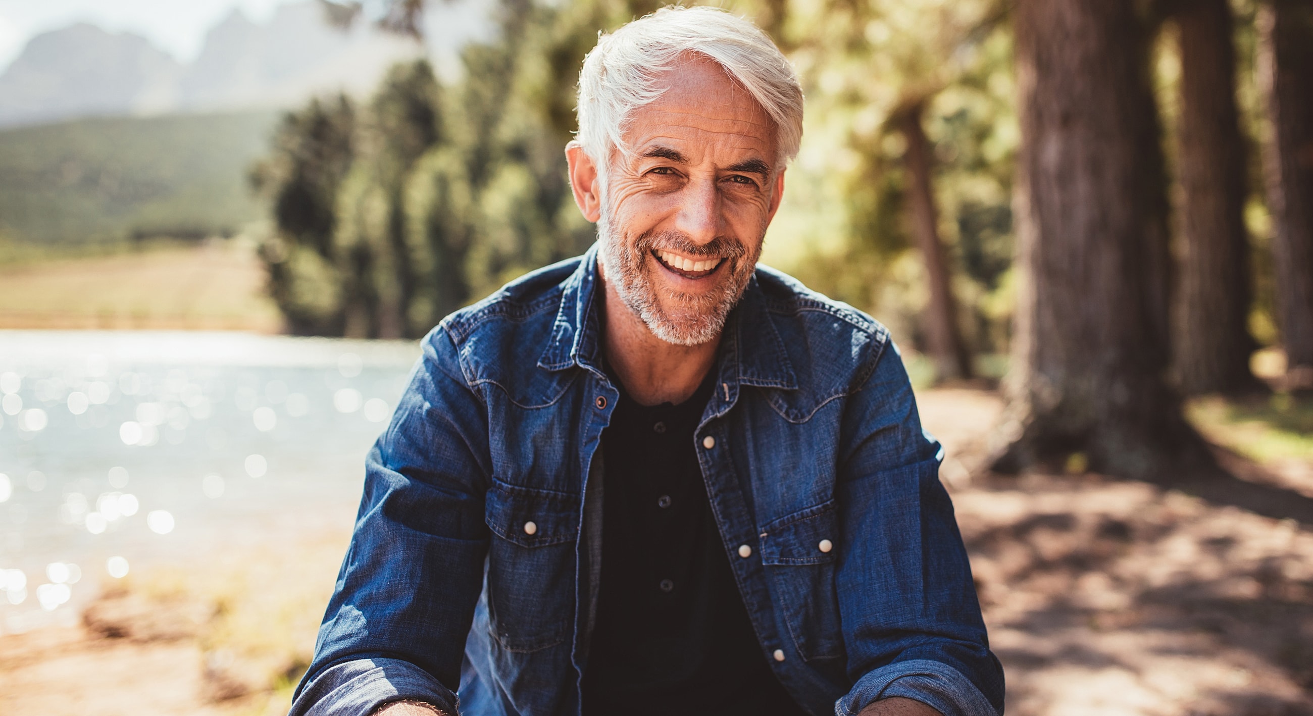 Smiling man by a lake in natural setting.